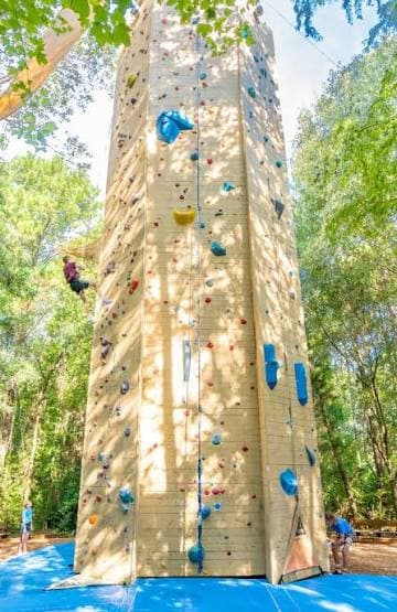 Climbers on the outdoor climbing tower at Palmetto Peaks, surrounded by trees